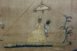 Detail of embroidery depicting a richly dressed woman under a parasol held by a black boy