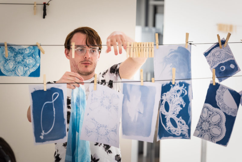 Student pins up his cyanotype print next to other prints on a washing line