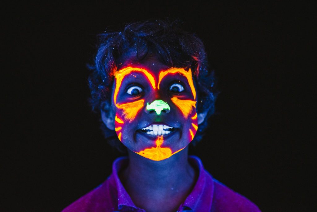 A child in a dark room wearing orange glow in the dark face paint