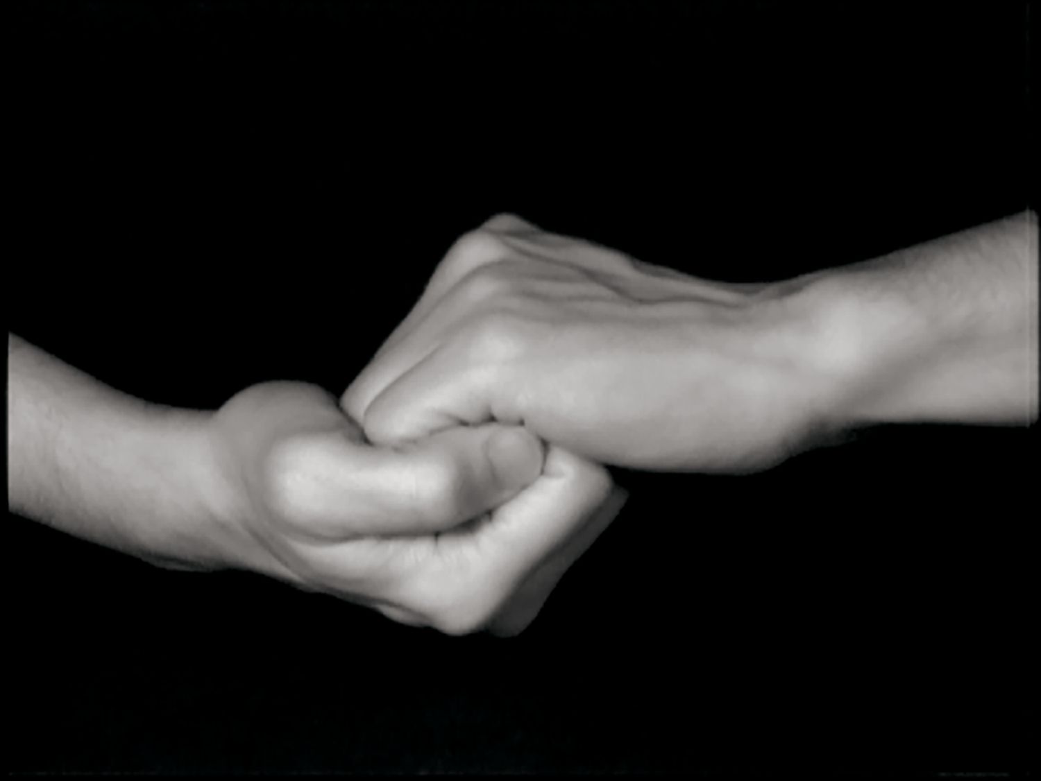 black and white image of two hands clasping in front of a black background