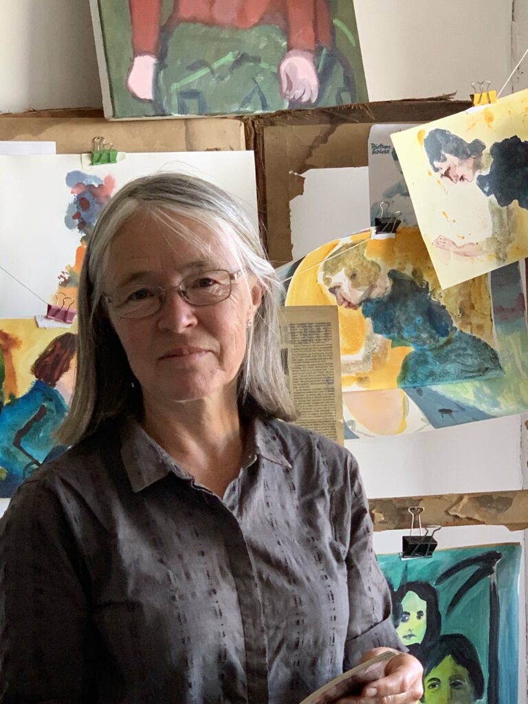 Janet Sainsbury standing in front of paintings in her studio