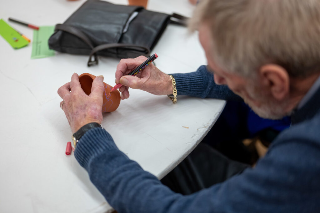 an older gentleman decorating a small clay pot with an acrylic marker
