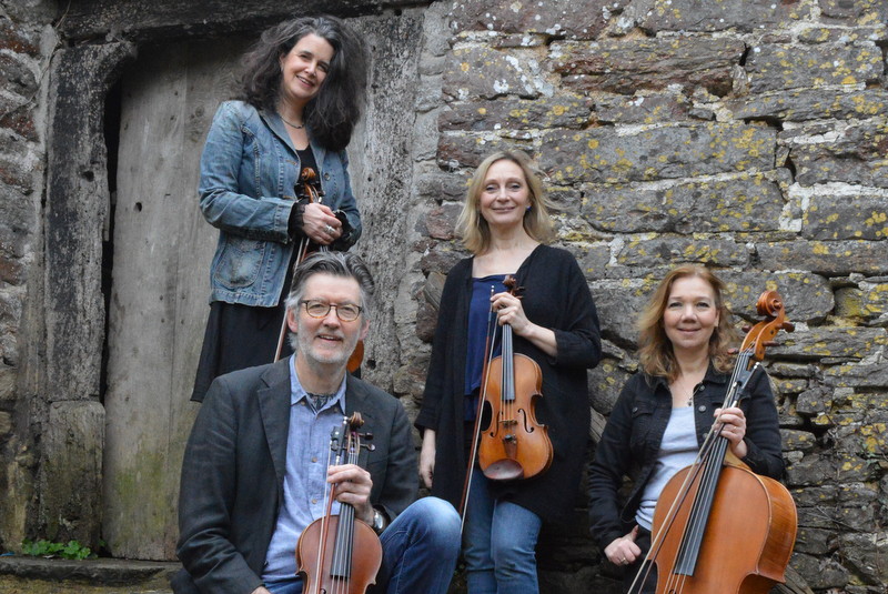 Four musicians holding their violins/viola/cello for the Christmas concert, standing against a stone wall