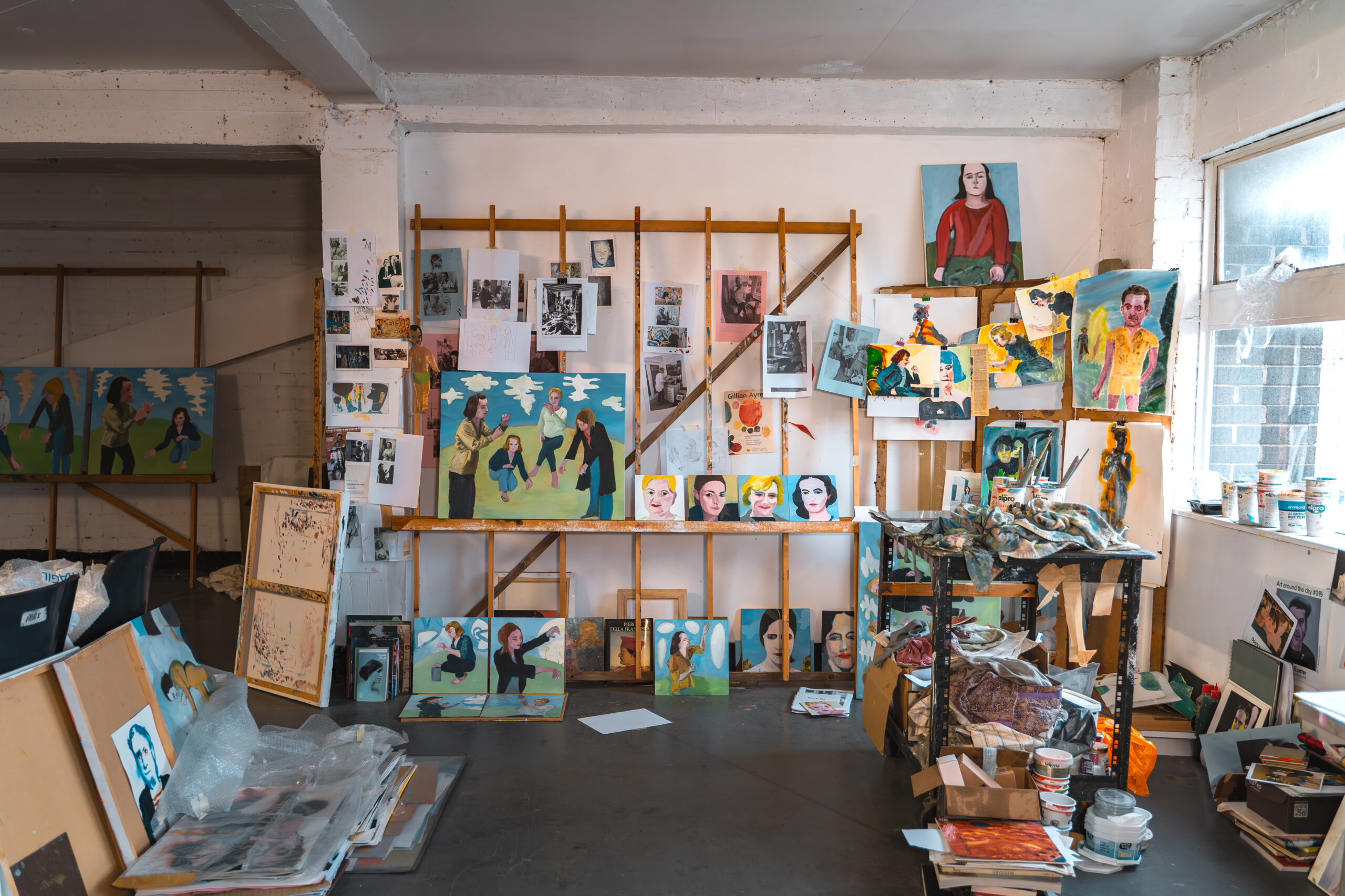 Janet Sainsbury's studio - a large room with a rack leaning against a wall, from which colourful paintings of figures are hanging