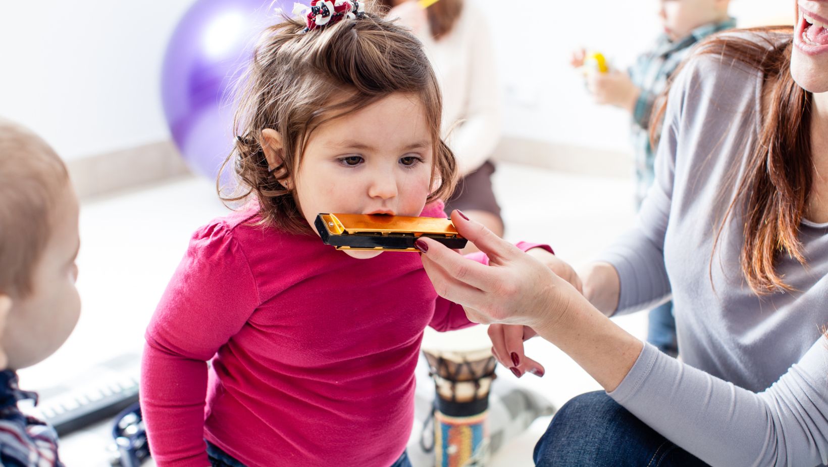 Image of a toddler girl with brown hair blowing into a harmonica