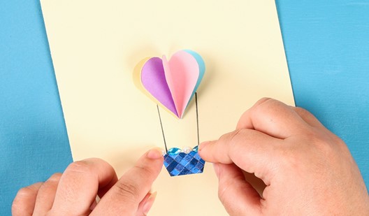 Photo of hands making a small hot air balloon out of coloured paper