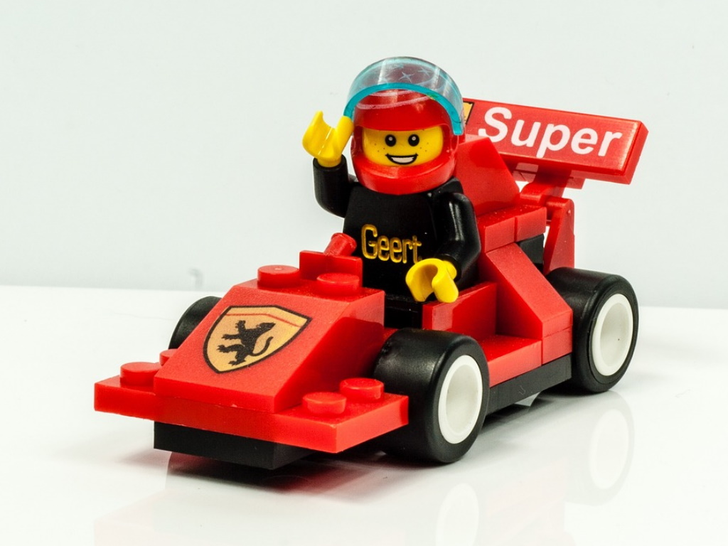 Photo of a small red racing car made out of Lego bricks with a mini-figure waving