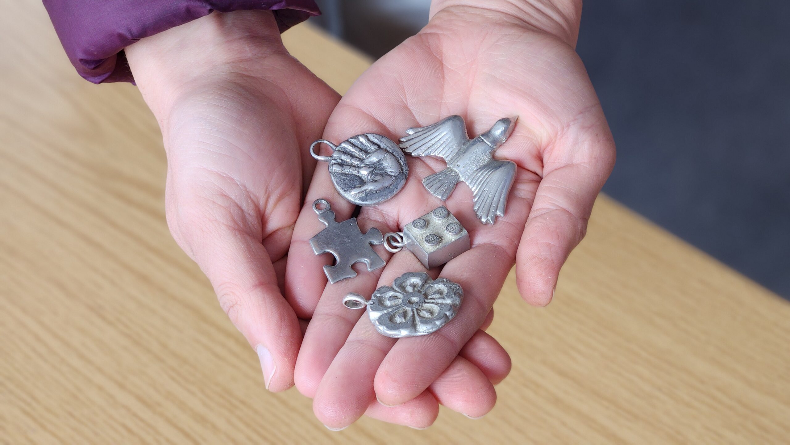 Photo of a person's hands holding a selection of small metal objects including a coin, a bird and a Lego brick