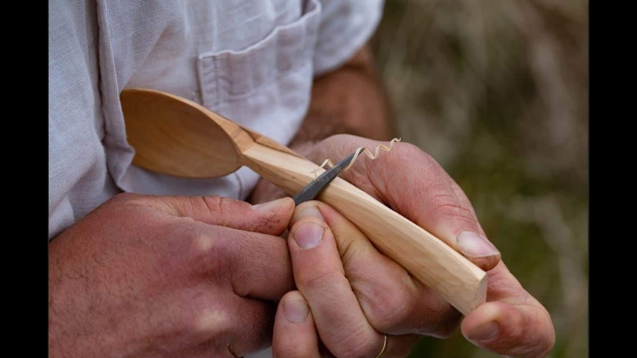 close up of a man's hands, carving a spoon out of a branch of wood
