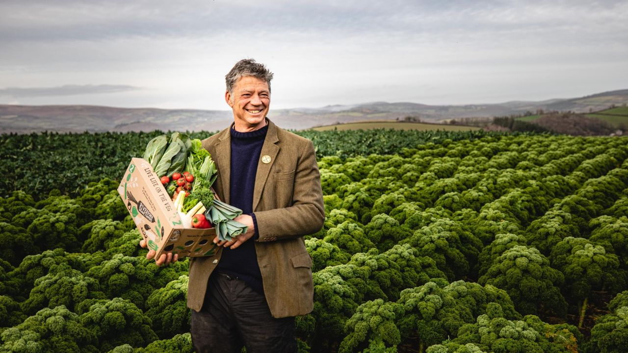 Guy, founder of Riverford, standing in a field holding a box of vegetables.