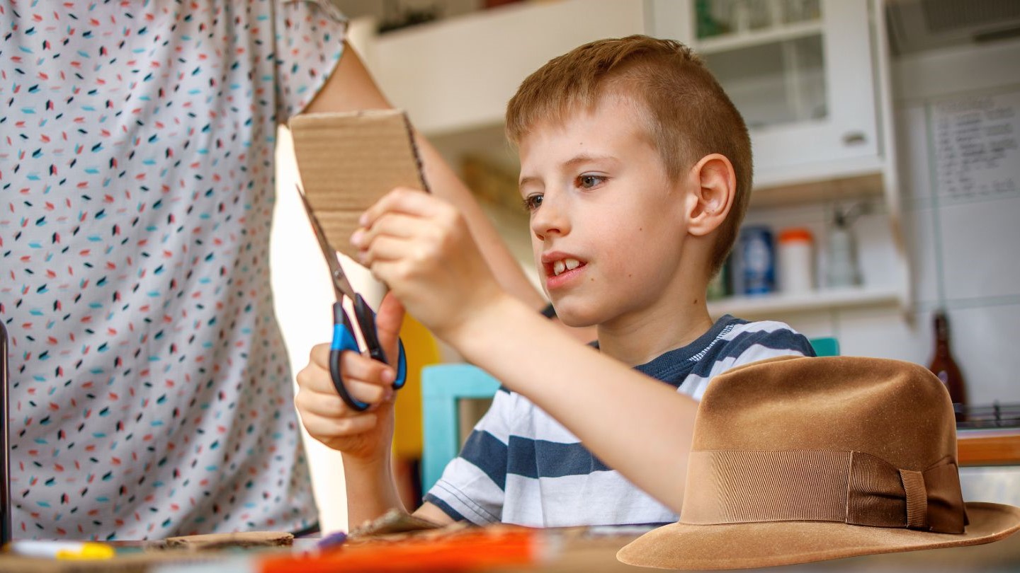 Photo of a young blond boy, about 7 years old, cutting out a shape from cardboard.