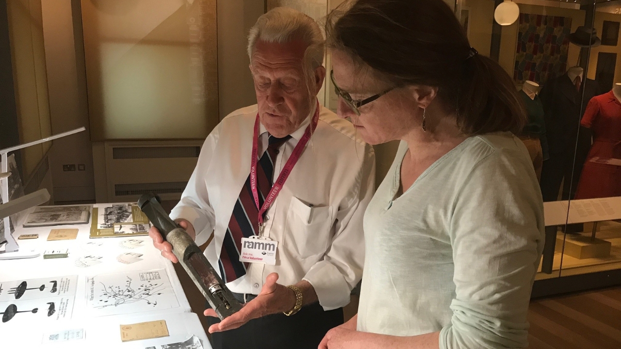 an older male volunteer at RAMM showing an artefact to a younger woman